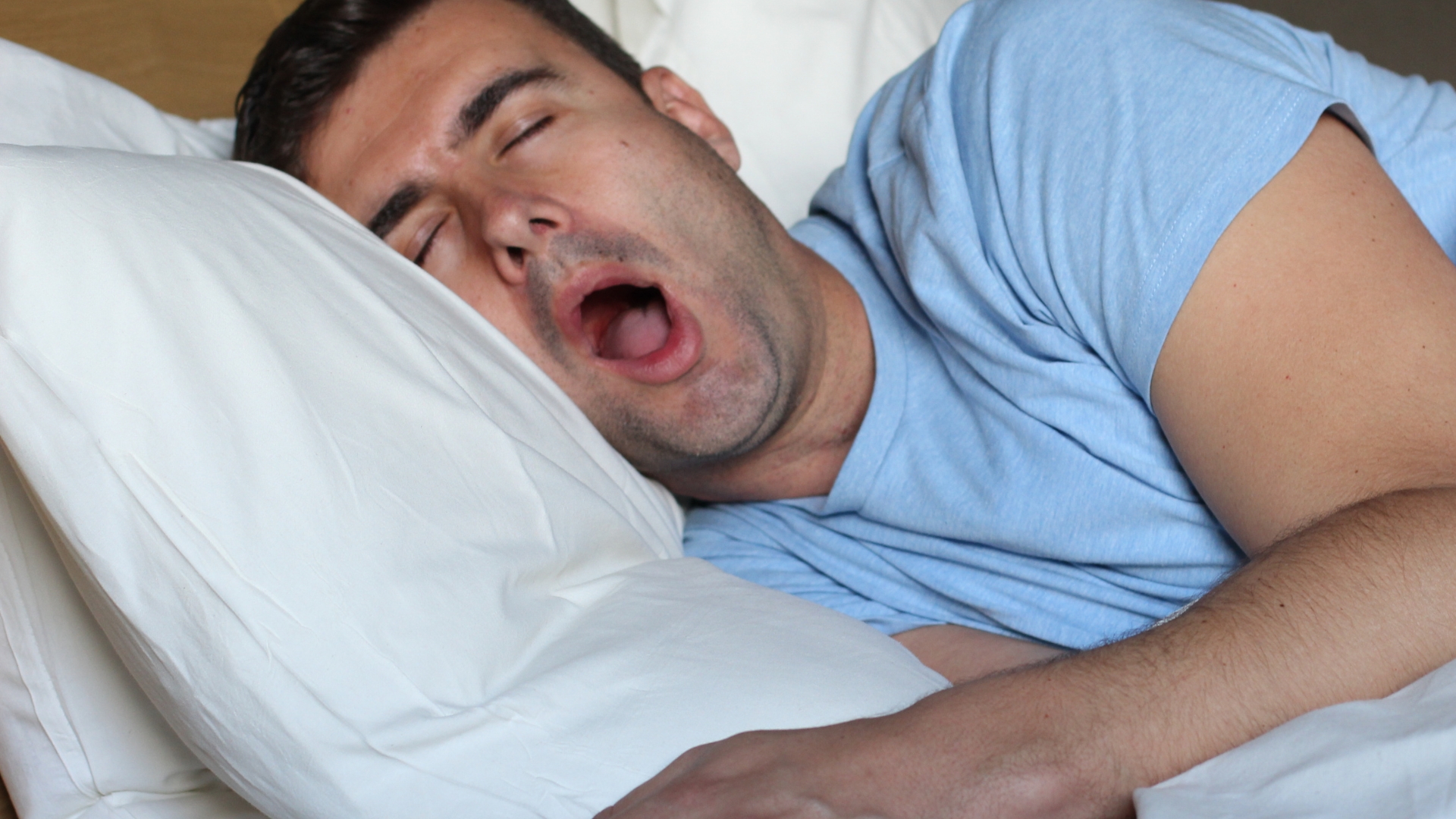 Man snoring heavily in bed at night while his partner lies awake beside him