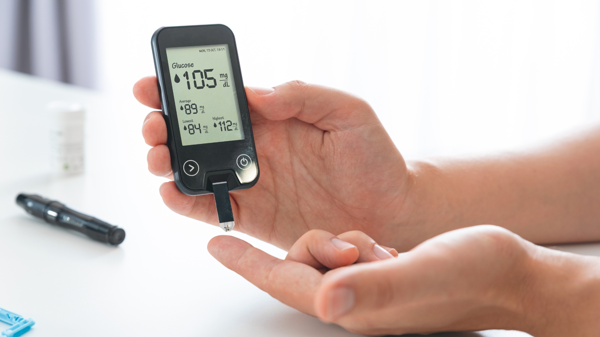 Person checking their blood glucose level with a glucometer beside a healthy meal